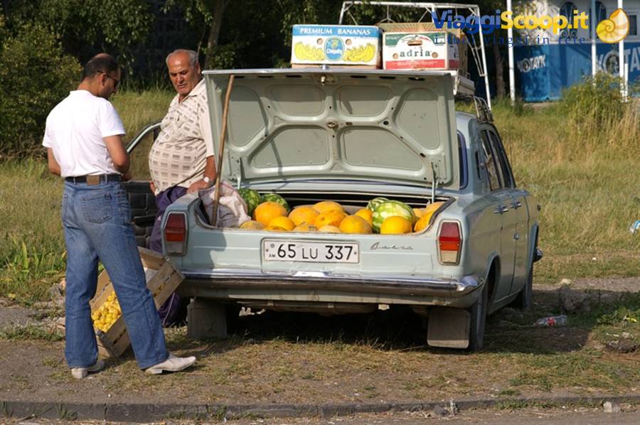 Two men selling melons and watermelons from a car trunk