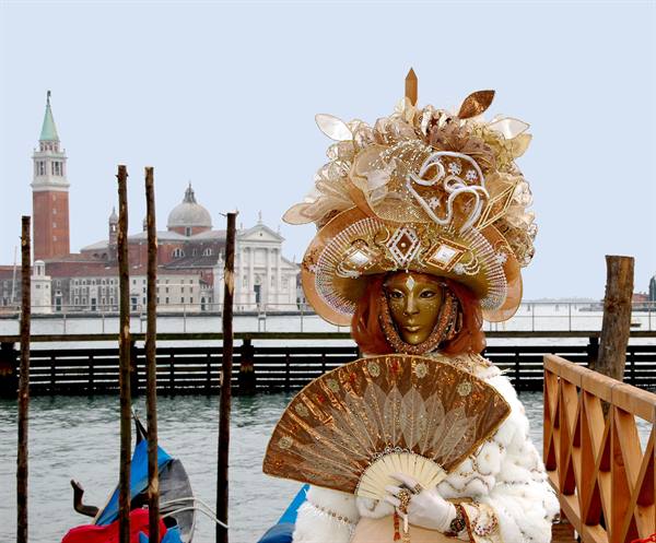 Golden masked figure with fan at Venice Carnival, San Giorgio Maggiore in the background