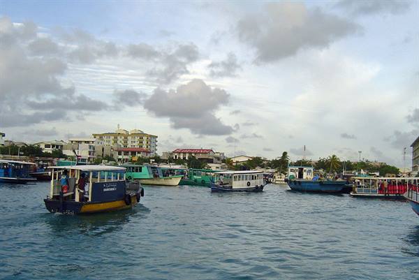 Ferries and speedboats moored at Malé harbor among low buildings under cloudy sky