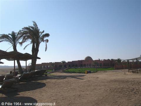 Sandy beach with straw umbrellas, palm trees and domed resort under blue sky