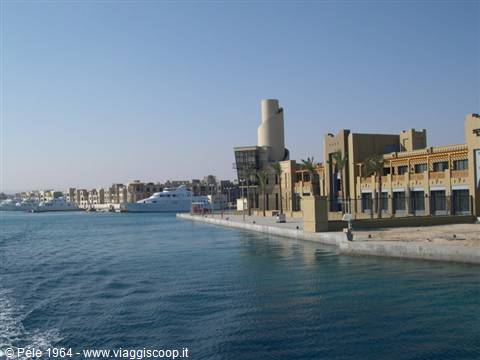 Marina with moored yachts and sand-colored buildings under a blue sky