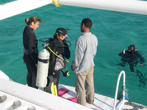 Divers with scuba tank and wetsuit prepare to dive from boat into turquoise sea