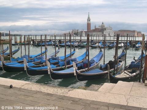 Black gondolas covered in blue tarps moored in Venice, San Giorgio Maggiore behind
