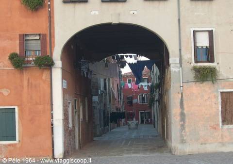 Stone arch over a narrow alley with laundry hung between colored houses
