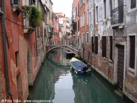 Venice canal with covered boats and stone bridge between faded facades