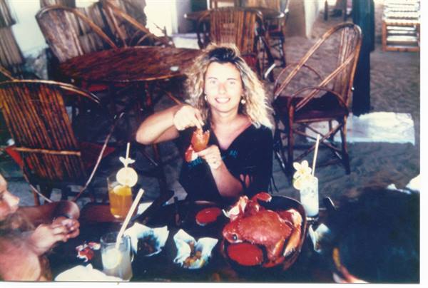 Smiling woman eating crab at a wicker restaurant table on sand
