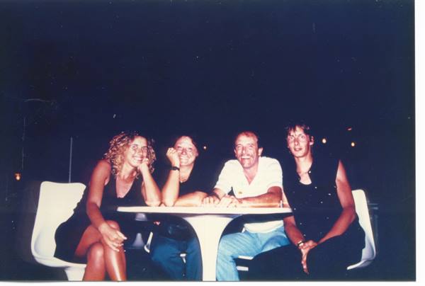 Four friends sitting at a white table on a terrace, lit by nighttime flash