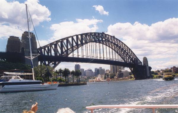 Sydney Harbour Bridge steel arch seen from ferry, white yacht and skyscrapers