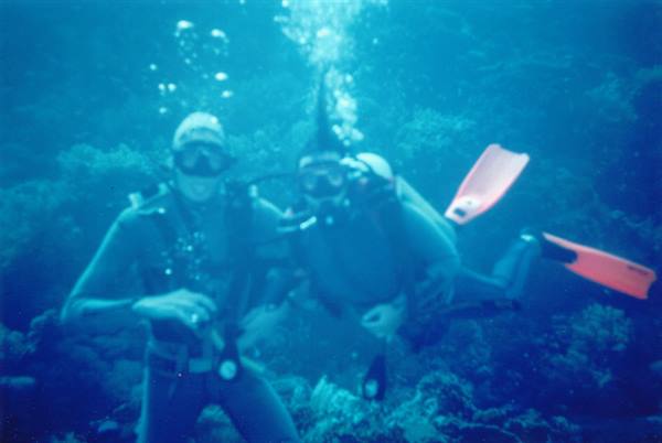 Two scuba divers with pink fins among corals, bubbles rising underwater