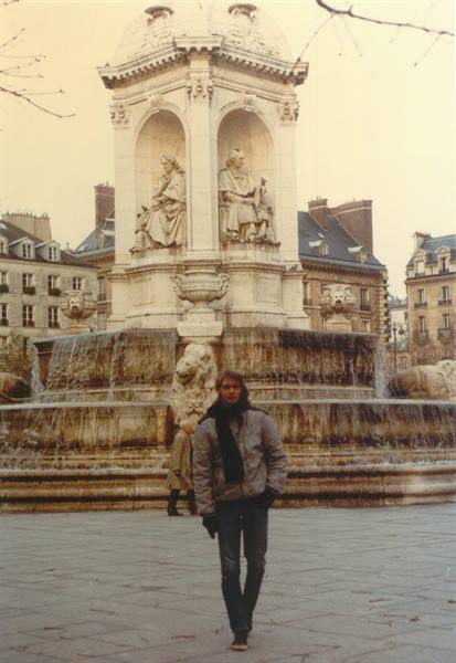 Young man in gray jacket walks past the Saint-Sulpice fountain in Paris