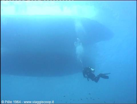 Scuba diver swims underwater near a large ship hull