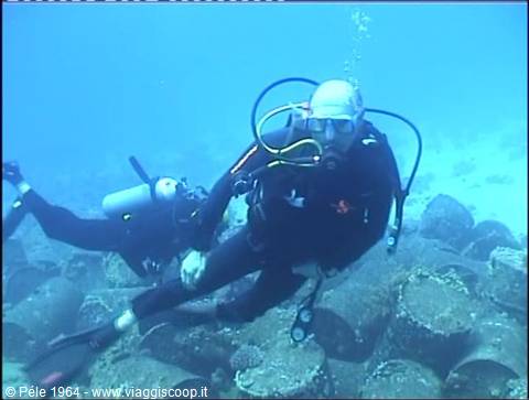 Two scuba divers with oxygen tanks swim over rocky underwater seabed