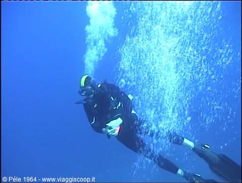 scuba diver in black wetsuit ascending among air bubbles in deep blue sea