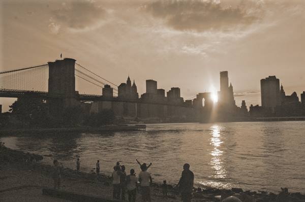 Tourists on the East River shore before Brooklyn Bridge and Manhattan skyline