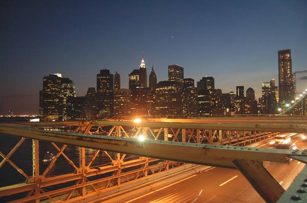 Steel truss of Brooklyn Bridge at dusk, Manhattan's illuminated skyscrapers behind