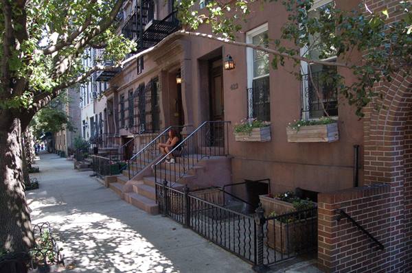 Woman sitting on brownstone stoop steps, dappled tree shade