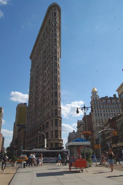 Flatiron Building in New York, brick facade under blue sky, pedestrians and food cart
