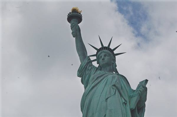 Copper verdigris Statue of Liberty raising her torch against cloudy skies