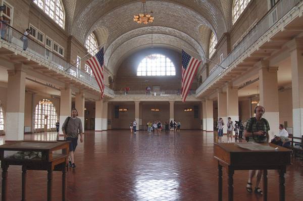 Ellis Island registry hall: brick vaulted ceiling, American flags, visitors among wooden desks