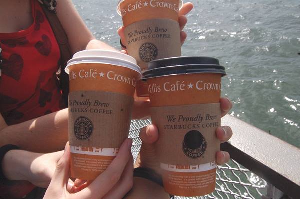 Three Starbucks coffee cups raised by the sea in sunlight