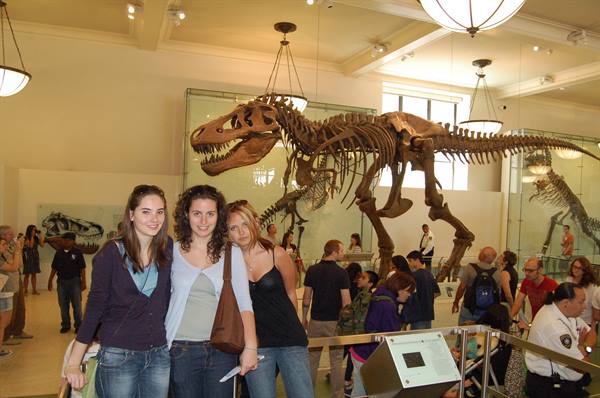 Three girls pose beside a T-Rex skeleton in the natural history museum