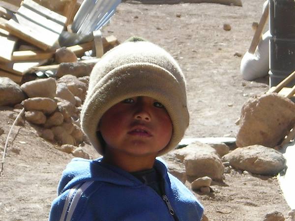 Child in wool hat and blue jacket among rocks and lumber in bright sunlight