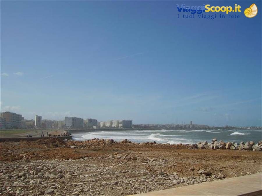 Ocean waves before the city buildings, rocky shore in the foreground