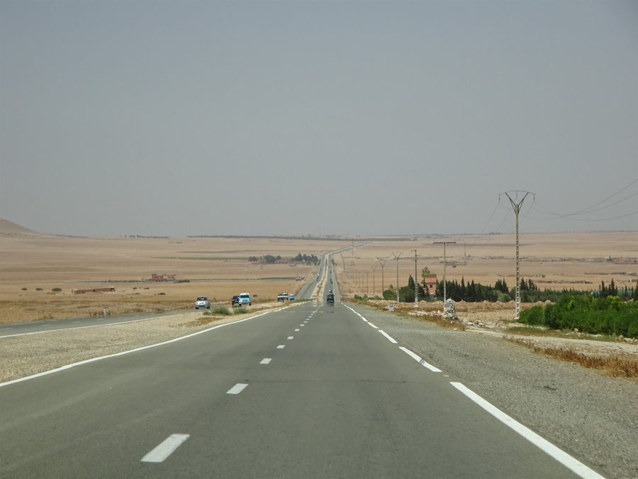 Straight desert highway toward Errachidia, cars and power poles among arid fields