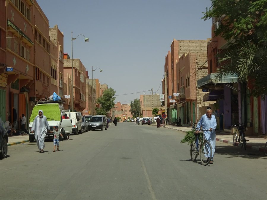 Man in blue djellaba pushing bicycle along shaded street in Ouarzazate