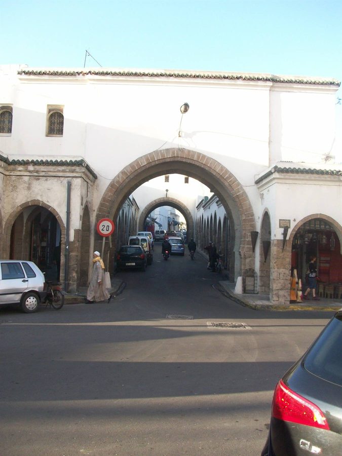 Stone arched gate over a street with cars and pedestrians in Essaouira medina